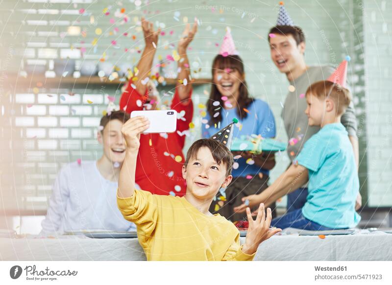 Mutter und Söhne feiern den Geburtstag ihrer Großmutter in ihrer Küche, der Junge macht Selfies Generation Confetti Telekommunikation telefonieren Handies