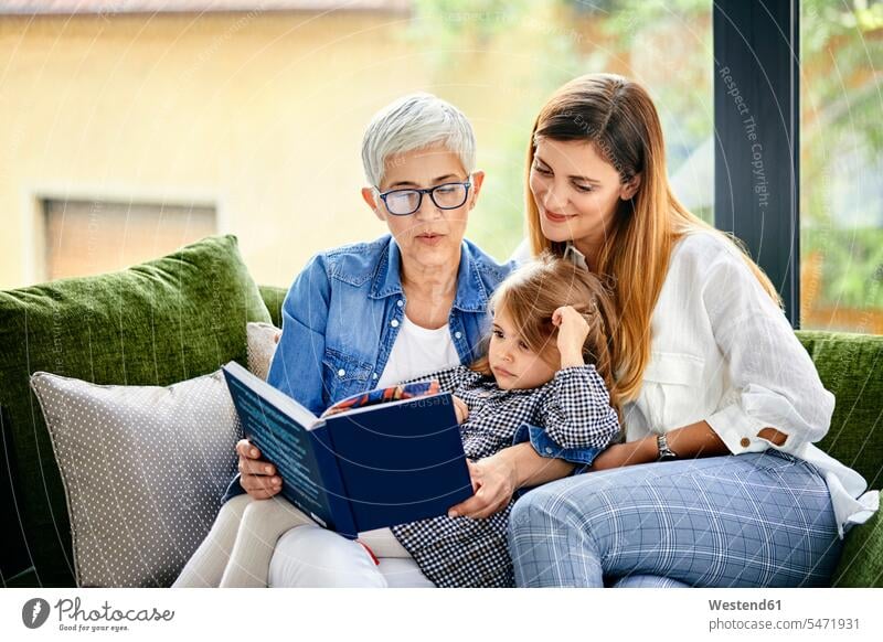 Mutter, Tochter und Enkelin sitzen auf der Couch und lesen ein Buch Leute Menschen People Person Personen Europäisch Kaukasier kaukasisch erwachsen Erwachsene