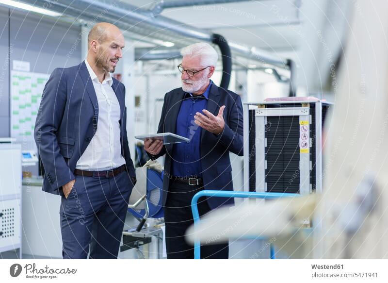 Leitender männlicher Manager diskutiert mit einem Kollegen über ein digitales Tablett, während er in der Fabrik an der Maschine steht Farbaufnahme Farbe