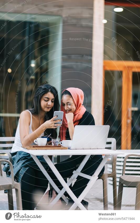 Zwei Freunde sitzen zusammen auf einem Bürgersteig Cafe mit Handy Laptop benutzen Laptop benützen Tisch Tische Instant Messaging Messenger sitzend sitzt