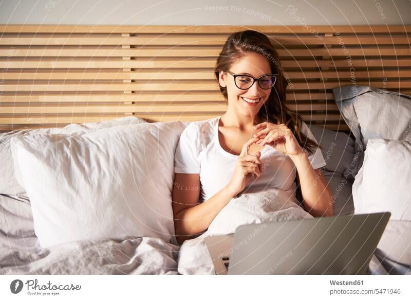 Porträt einer lächelnden jungen Frau auf dem Bett liegend mit Laptop Betten benutzen benützen liegt weiblich Frauen Portrait Porträts Portraits Notebook Laptops