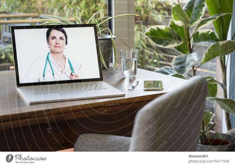 Weiblicher Arzt auf Laptop-Bildschirm für Videoanruf zu Hause Farbaufnahme Farbe Farbfoto Farbphoto Innenaufnahme Innenaufnahmen innen drinnen Tag