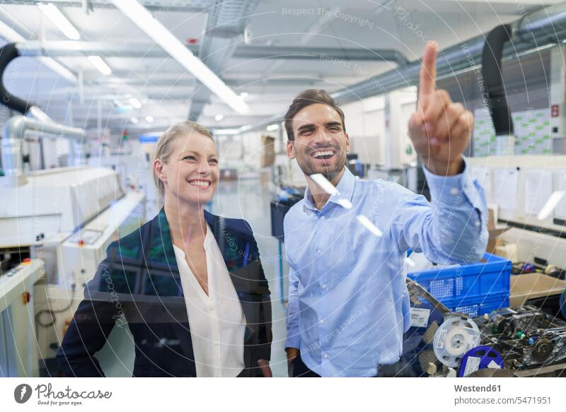Glücklicher junger männlicher Techniker zeigt auf grafische Oberfläche auf Glas in der Fabrik Farbaufnahme Farbe Farbfoto Farbphoto Innenaufnahme Innenaufnahmen