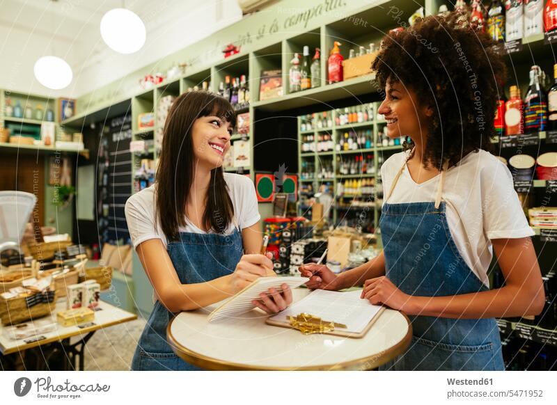 Zwei lächelnde Frauen in einem Geschäft, die Notizen machen weiblich notieren Shop Laden Läden Geschäfte Shops Erwachsener erwachsen Mensch Menschen Leute