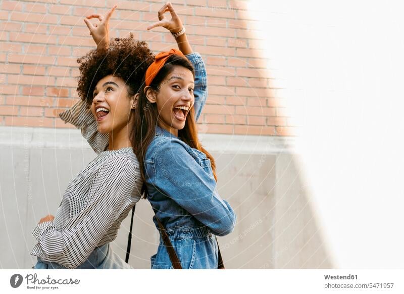 Fröhliche Freunde zeigen aufeinander zu, während sie mit dem Rücken zur Wand stehen Farbaufnahme Farbe Farbfoto Farbphoto Außenaufnahme außen draußen im Freien