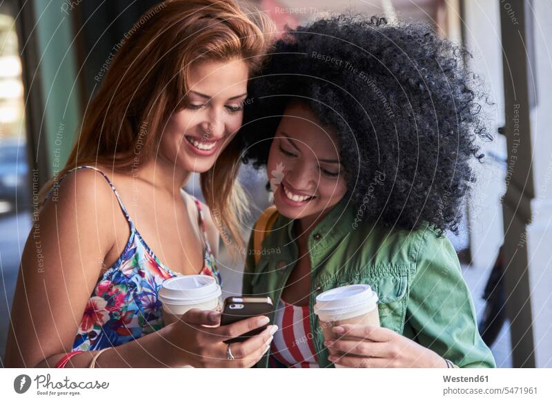 Freundinnen mit Kaffee zum Mitnehmen mit Smartphone Telekommunikation telefonieren Handies Handys Mobiltelefon Mobiltelefone freuen Glück glücklich sein