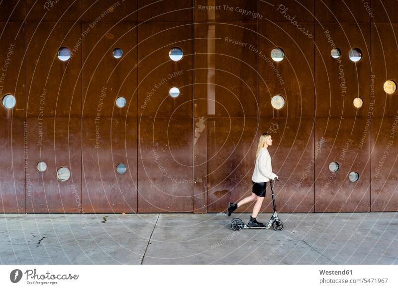 Junge Frau mit Kickroller in der Stadt Tretroller Muße Lifestyles außen draußen im Freien staedtisch städtisch Urbanitaet Urbanität auf Achse in Bewegung