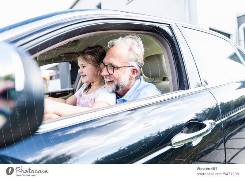 Kleines Mädchen sitzt auf dem Schoß des Großvaters und gibt vor, das Auto zu lenken Wagen PKWs Automobil Autos Sommer Sommerzeit sommerlich autofahren spielen