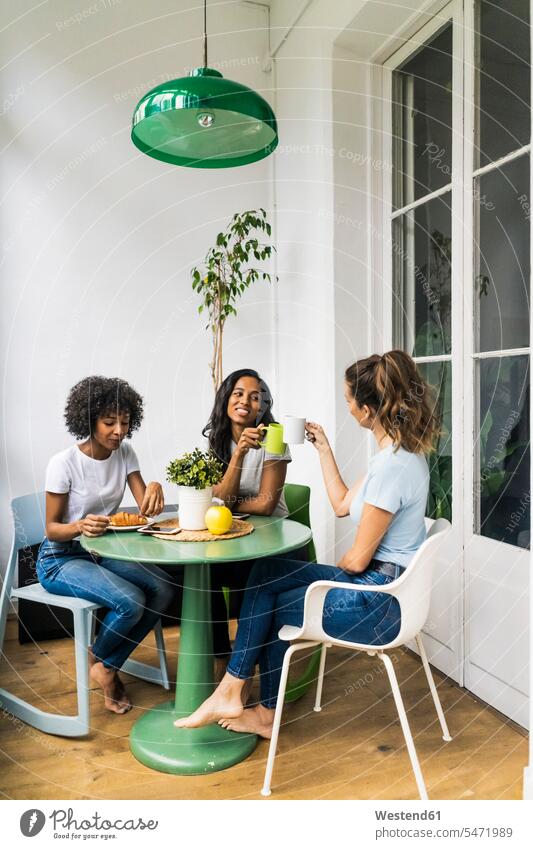 Drei glückliche Frauen sitzen am Tisch zu Hause trinken Kaffee zusammen sitzend sitzt Tische Freundinnen Glück glücklich sein glücklichsein Gemeinsam Zusammen
