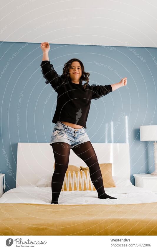 Fröhliche junge Frau mit Down-Syndrom tanzt zu Hause auf dem Bett Europäer Europäisch Kaukasier kaukasisch eine Person ein Mensch nur eine Person