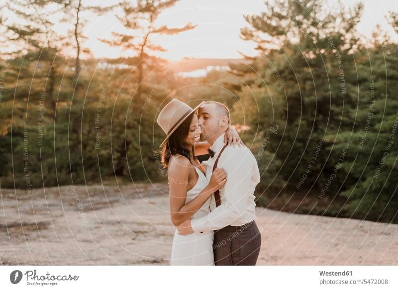 Ein Paar küsst sich, während es bei Sonnenuntergang auf einem Waldweg steht Farbaufnahme Farbe Farbfoto Farbphoto Außenaufnahme außen draußen im Freien
