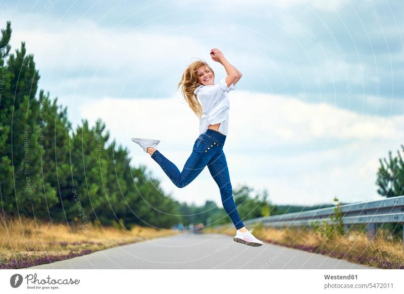 Fröhliche Frau springt auf Landstraße Touristen Hosen Jeanshose sommerlich Sommerzeit entspannen relaxen entspanntheit relaxt freuen Frohsinn Fröhlichkeit