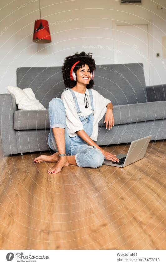 Glückliche Frau sitzt zu Hause mit Kopfhörer und Laptop glücklich glücklich sein glücklichsein Zuhause daheim weiblich Frauen sitzen sitzend Notebook Laptops