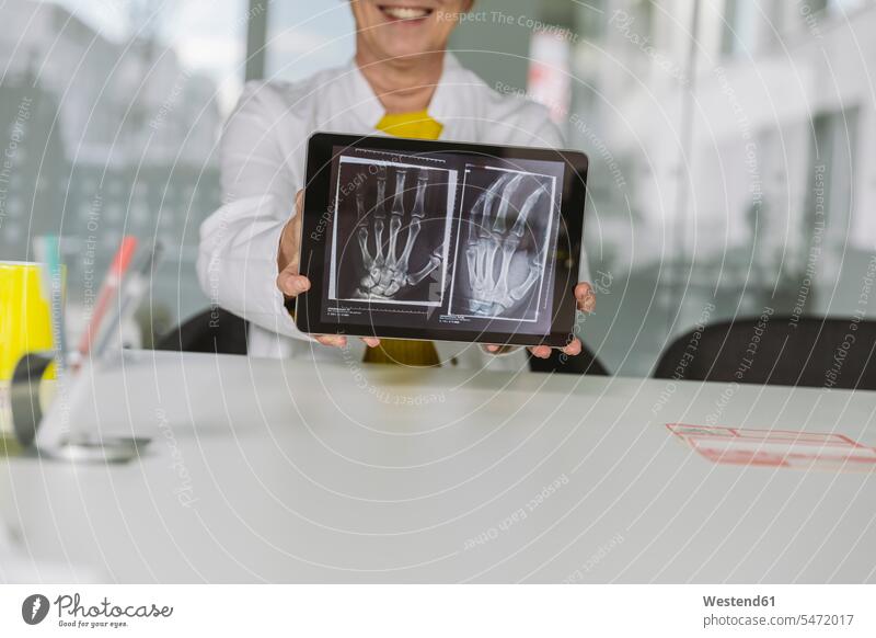 Am Schreibtisch sitzender Arzt zeigt Röntgenbild der Hand auf digitalem Tablett Job Berufe Berufstätigkeit Beschäftigung Jobs Bilder Bildnis Roentgenbild