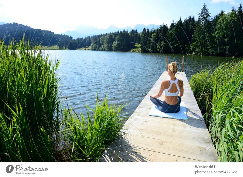 Deutschland, Mittenwald, Rückenansicht einer Frau, die auf einem Steg am See Yoga praktiziert Rückansicht Rueckansicht Rueckenansicht von hinten üben ausüben