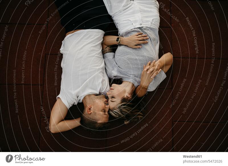 Auf dem Boden liegendes junges Paar, von oben entspannen relaxen knuddeln schmusen Arm umlegen Umarmung Umarmungen abends freuen Glück glücklich sein