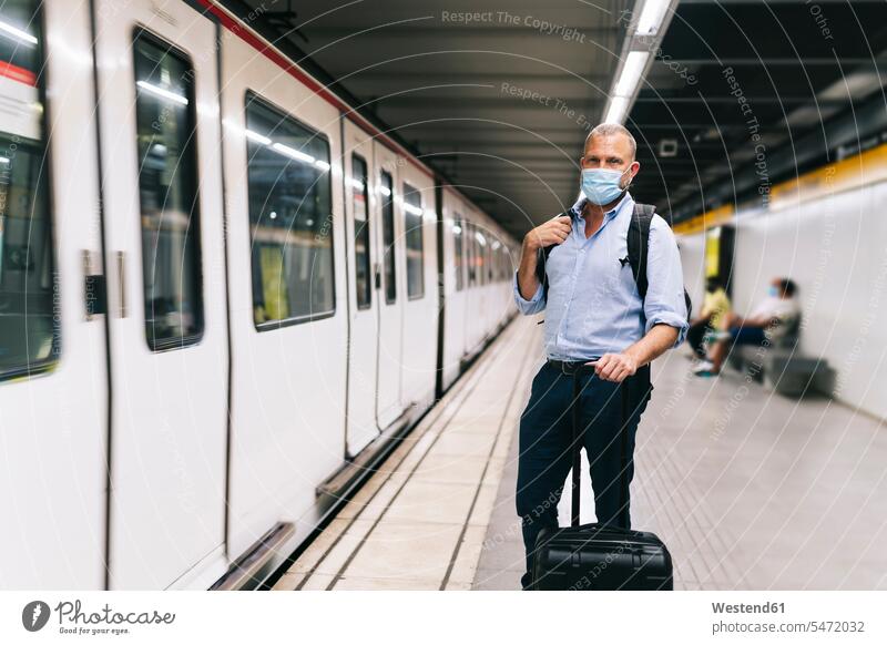 Geschäftsmann mit Gesichtsmaske, während er mit Gepäck am U-Bahnsteig steht Geschäftsleute Geschäftsperson Geschäftspersonen Business Geschäftsleben