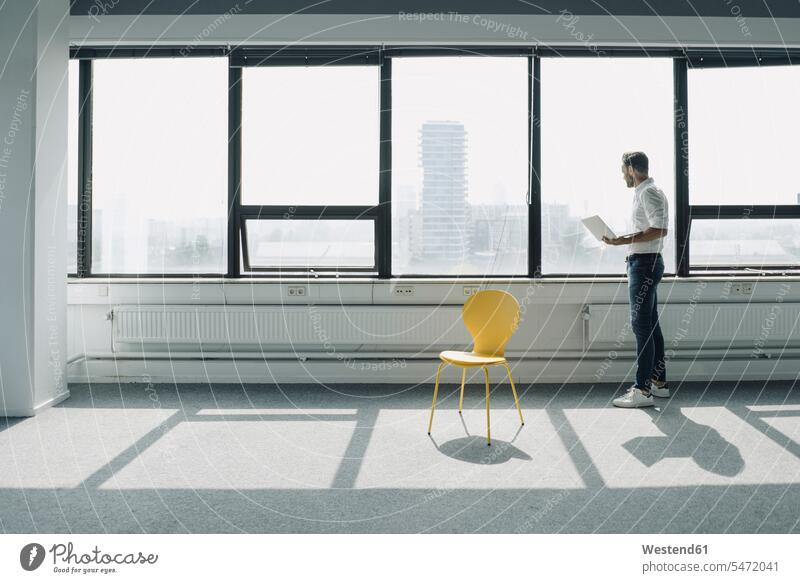 Reifer Geschäftsmann mit Laptop am Fenster im leeren Büro Job Berufe Berufstätigkeit Beschäftigung Jobs geschäftlich Geschäftsleben Geschäftswelt