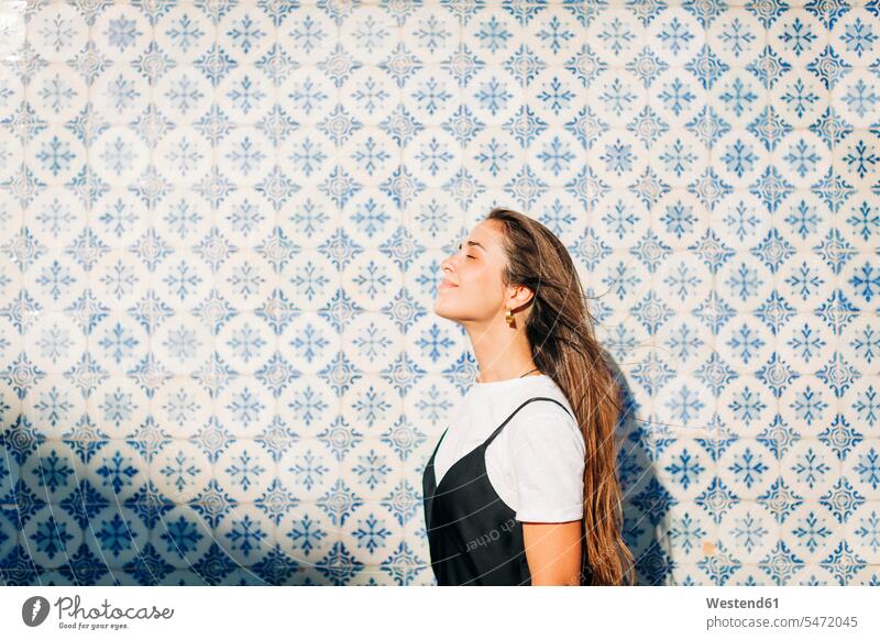 Lächelnde schöne Frau mit geschlossenen Augen steht an der gekachelten Wand an einem sonnigen Tag Farbaufnahme Farbe Farbfoto Farbphoto Portugal