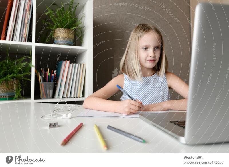Mädchen, das zu Hause am Tisch sitzt, Hausaufgaben macht und einen Laptop benutzt Stift lernen lächeln schreiben sitzen Zufriedenheit Zuhause Internet