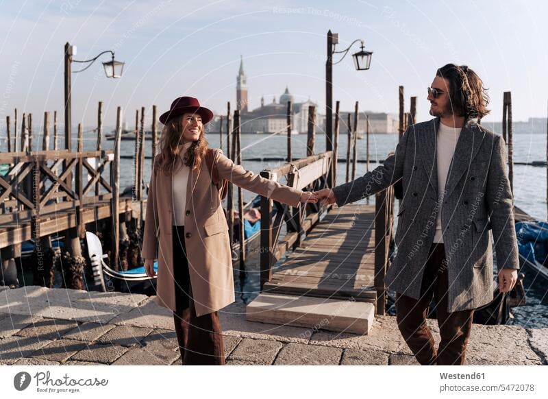 Junges Paar geht Hand in Hand an der Uferpromenade von Venedig, Italien Hüte Jacken Brillen Sonnenbrillen gehend freuen geniessen Genuss Glück glücklich sein