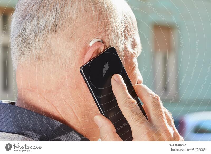 Nahaufnahme eines älteren Mannes mit Hörgerät per Smartphone Hörgeräte Hoergeraet Hoergeraete telefonieren anrufen Anruf telephonieren iPhone Smartphones Senior