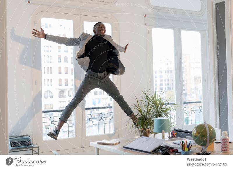 Glücklicher junger Geschäftsmann, der in seinem Büro in die Luft springt Luftsprung Luftsprünge einen Luftsprung machen Luftspruenge springen hüpfen glücklich