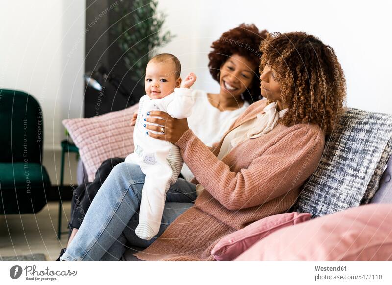 Lächelnde Familie sitzt mit Mädchen zu Hause auf dem Sofa Farbaufnahme Farbe Farbfoto Farbphoto Innenaufnahme Innenaufnahmen innen drinnen 2-5 Monate