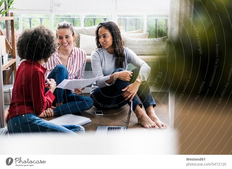 Drei Frauen mit Laptop und Dokumenten sitzen auf dem Boden zu Hause Böden Boeden glücklich Glück glücklich sein glücklichsein weiblich sitzend sitzt Unterlagen