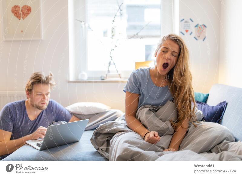 Junge Frau wacht zu Hause mit ihrem Partner am Laptop auf Leute Menschen People Person Personen Alleinstehende Alleinstehender Singles Unverheiratete