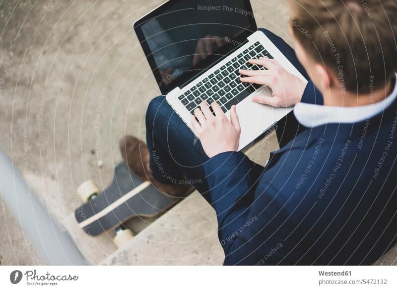 Junger Geschäftsmann mit Skateboard sitzt im Freien auf einer Treppe und benutzt einen Laptop Mann Männer männlich Businessmann Businessmänner Geschäftsmänner