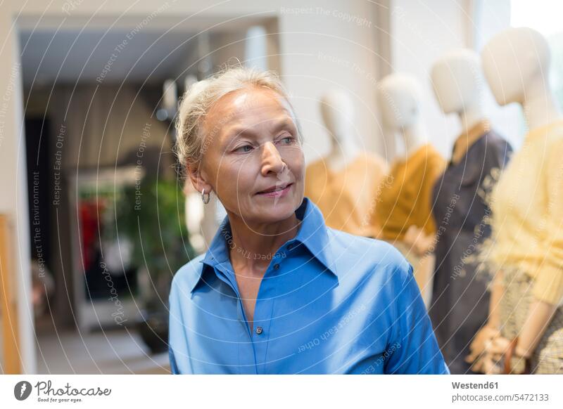 Lächelnde ältere Frau in einer Boutique, die sich umschaut Boutiquen weiblich Frauen Seniorin Seniorinnen alt umherblicken umschauen umsehen lächeln gespiegelt