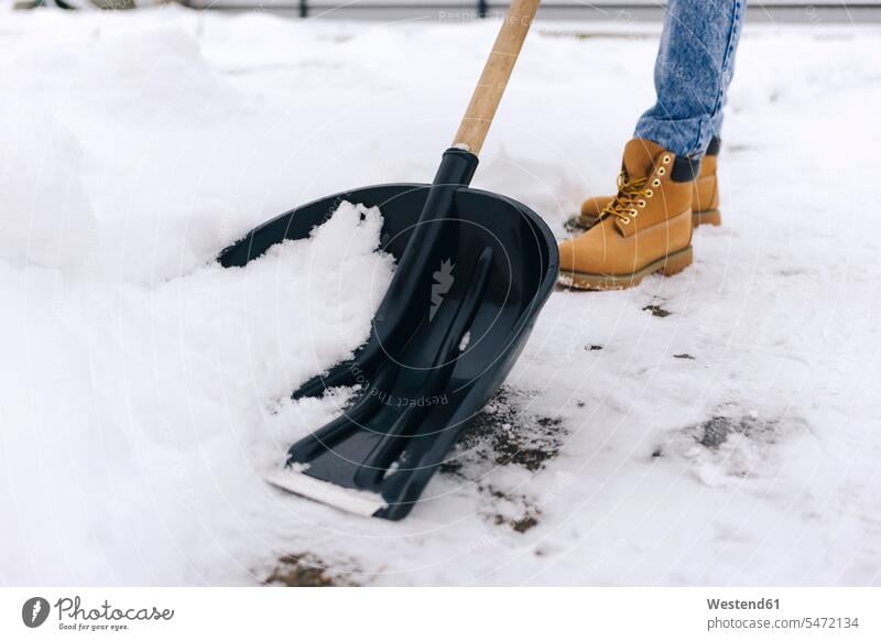 Schrägansicht einer Frau, die den Gehweg mit einer Schneeschaufel räumt Jahreszeiten winterlich Winterzeit stehend steht Kälte Muße Aktivitaet Aktivität Handeln