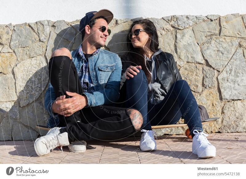 Junges verliebtes Paar sitzt Seite an Seite auf einem Longboard Brillen Sonnenbrillen sitzend freuen Glück glücklich sein glücklichsein gefühlvoll Emotionen