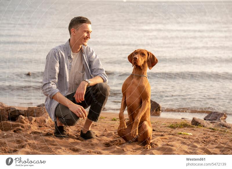 Junger Mann mit seinem Hund beim Training am Strand Tiere Tierwelt Haustiere Hunde abends Glück glücklich sein glücklichsein zufrieden stolz stolz sein Muße