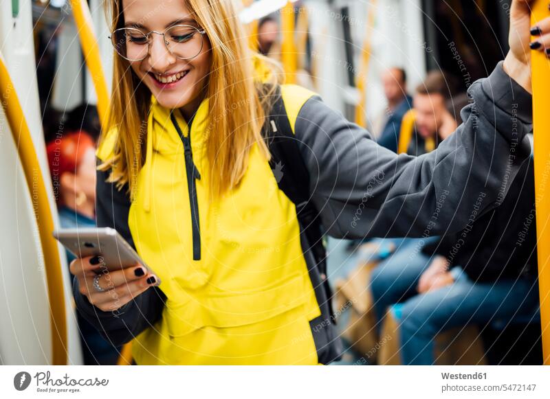Lächelnde junge Frau steht mit ihrem Smartphone in der U-Bahn Touristen Rucksäcke Transport Transportwesen Bahnen Subway U-Bahnen Ubahn Ubahnen Underground