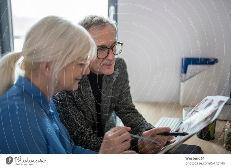 Zwei ältere Kollegen arbeiten gemeinsam am Schreibtisch im Büro und untersuchen Fotos Arbeitskollegen Senior ältere Männer älterer Mann Senioren mustern