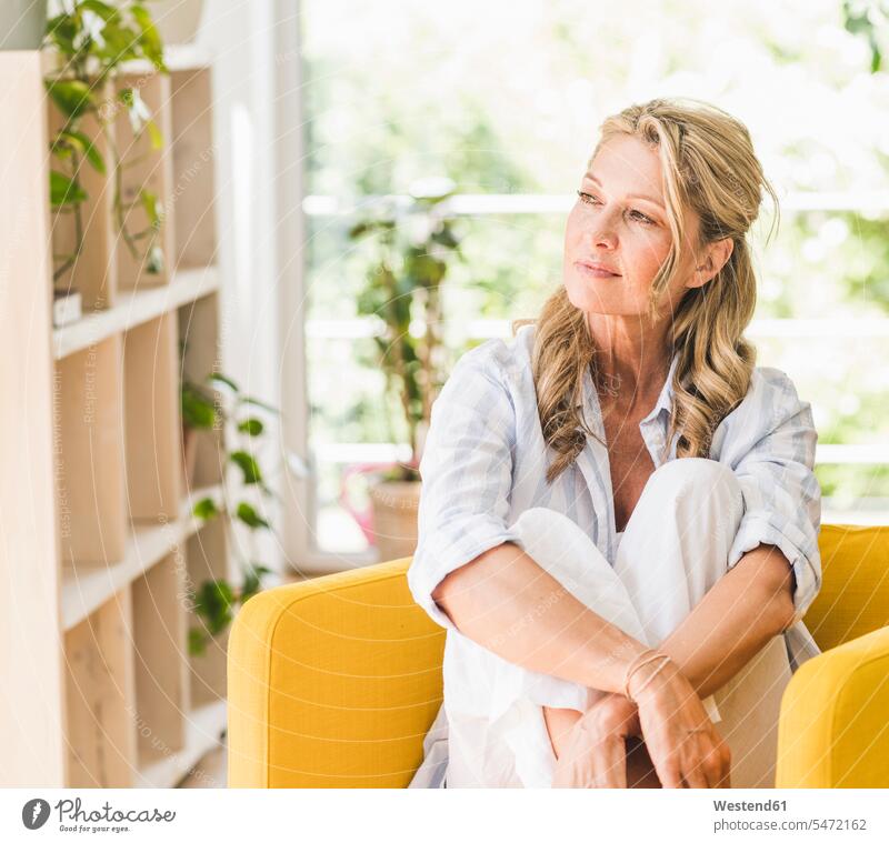 Porträt einer nachdenklichen reifen Frau zu Hause Ablage Regale entspannen relaxen sitzend sitzt Farben Farbtoene Farbton Farbtöne gelbe gelber gelbes daheim
