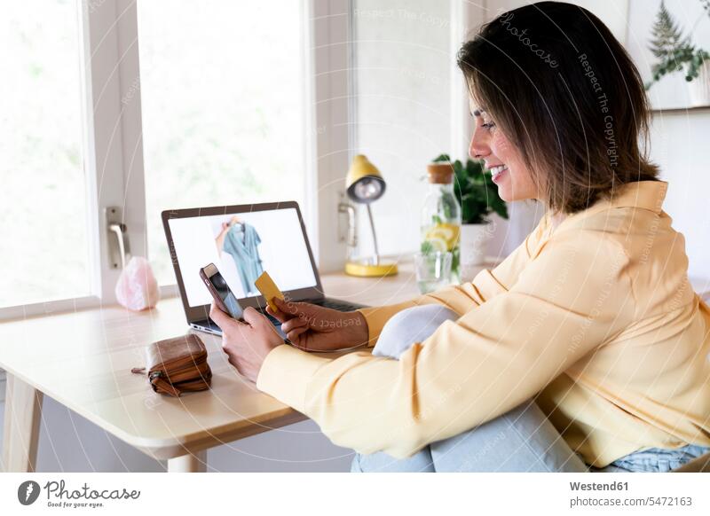 Glückliche junge Frau benutzt Kreditkarte und Smartphone für Online-Einkäufe zu Hause Farbaufnahme Farbe Farbfoto Farbphoto Spanien Innenaufnahme Innenaufnahmen