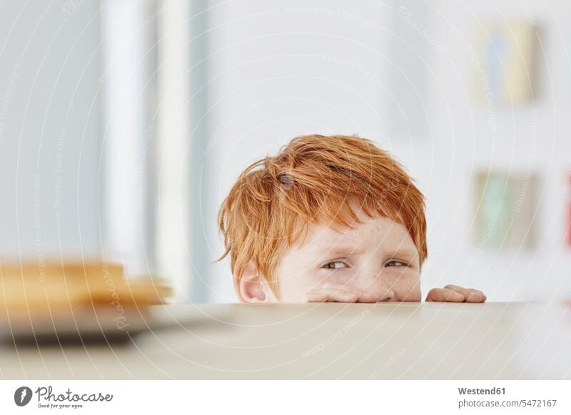 Porträt eines süßen Jungen zu Hause, der auf einen Teller auf dem Tisch schaut Koepfe Köpfe Gesichter Tische Gesichtsausdruck Mienenspiel daheim Wuensche