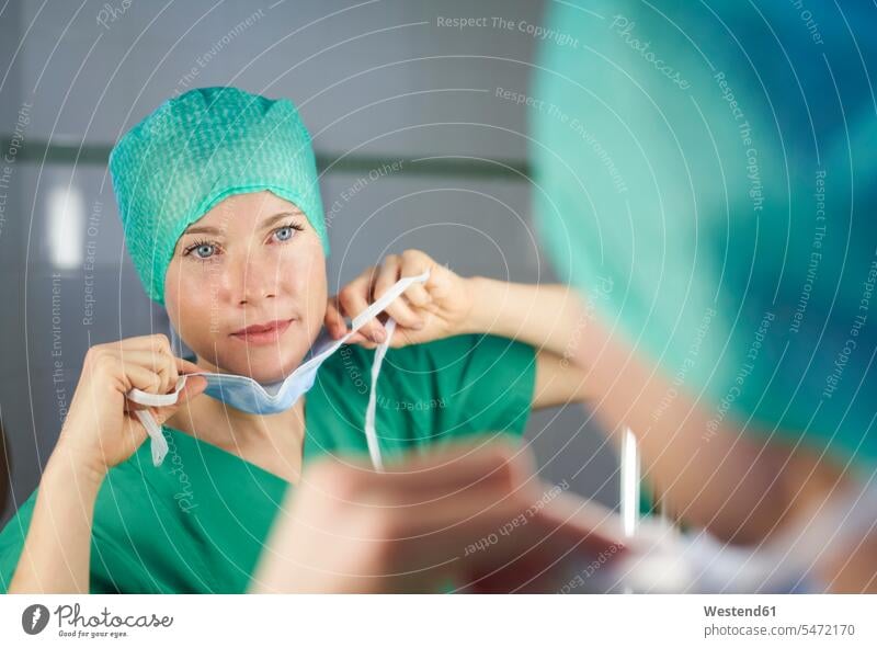 Frau in OP-Kleidung schaut in den Spiegel und setzt eine Maske auf Gesundheit Medizin medizinisch Gesundheitswesen betrachten betrachtend Sachverstand