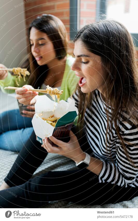 Zwei junge Frauen mit asiatischem Essen zum Mitnehmen zu Hause essen essend Zuhause daheim Asiatisch Freundinnen weiblich Freunde Freundschaft Kameradschaft