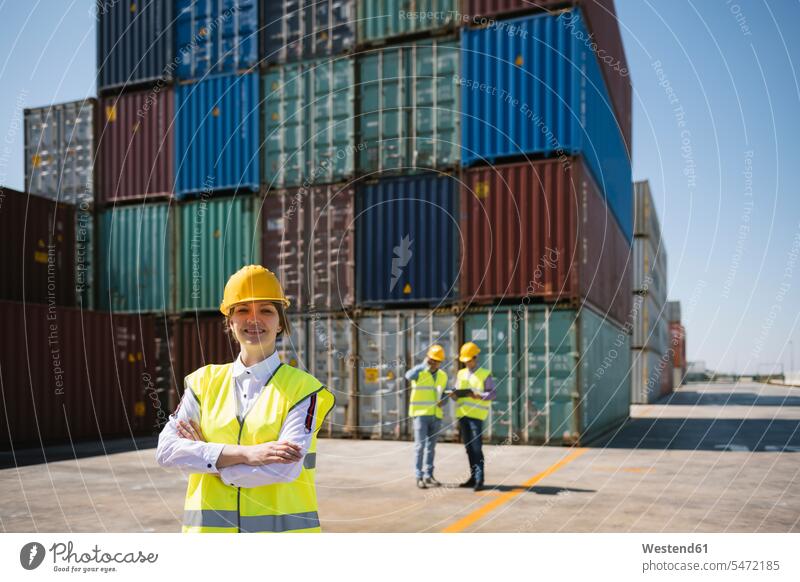 Porträt einer selbstbewussten Arbeiterin vor Kollegen und Frachtcontainern auf einem Industriegelände Hafengebiet Hafengebiete industriell Gewerbe Industrien