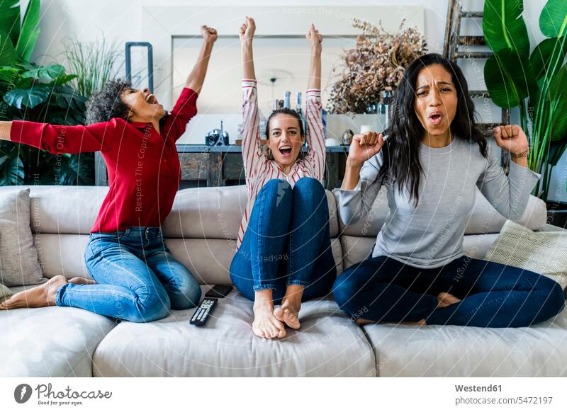 Drei aufgeregte Frauen auf der Couch zu Hause beobachten Tv und jubeln weiblich Zuhause daheim fernsehen glücklich Glück glücklich sein glücklichsein Aufregung