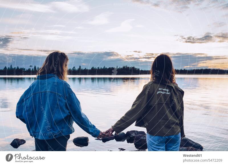 Freundinnen mit Blick auf den Inari-See, Finnland, halten Hände Seen sitzen sitzend sitzt junge Frau junge Frauen Hände halten Haendchen halten Hand halten