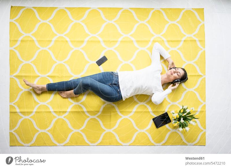 Lächelnde Frau mit Kopfhörern auf Teppich liegend mit Tulpenbüschel Blumenstrauß Bouquet Blumenstrauss Blumensträusse Blumensträuße liegt Tulipa