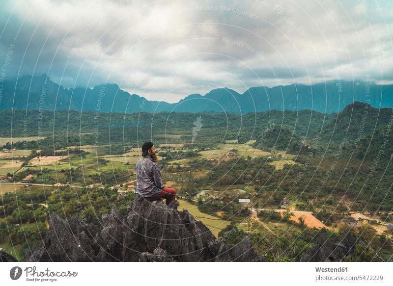 Laos, Vang Vieng, Wanderer auf Fels sitzend, Blick in die Ferne Freiheit frei Gipfel Berggipfel Aussicht bewundern die Aussicht bewundern Aussicht genießen