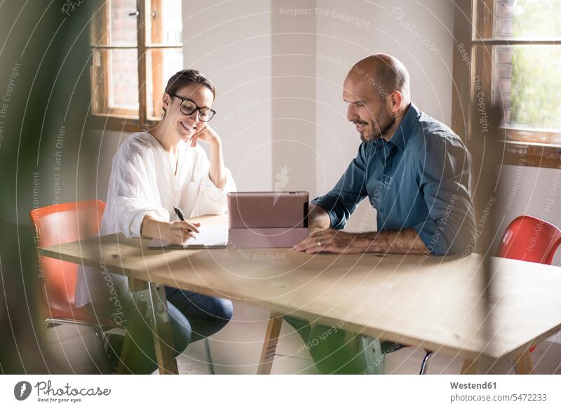 Geschäftsfrau schreibt auf dem Notizblock, während ein Mann mit einem digitalen Tablett im Büro sitzt Farbaufnahme Farbe Farbfoto Farbphoto Innenaufnahme