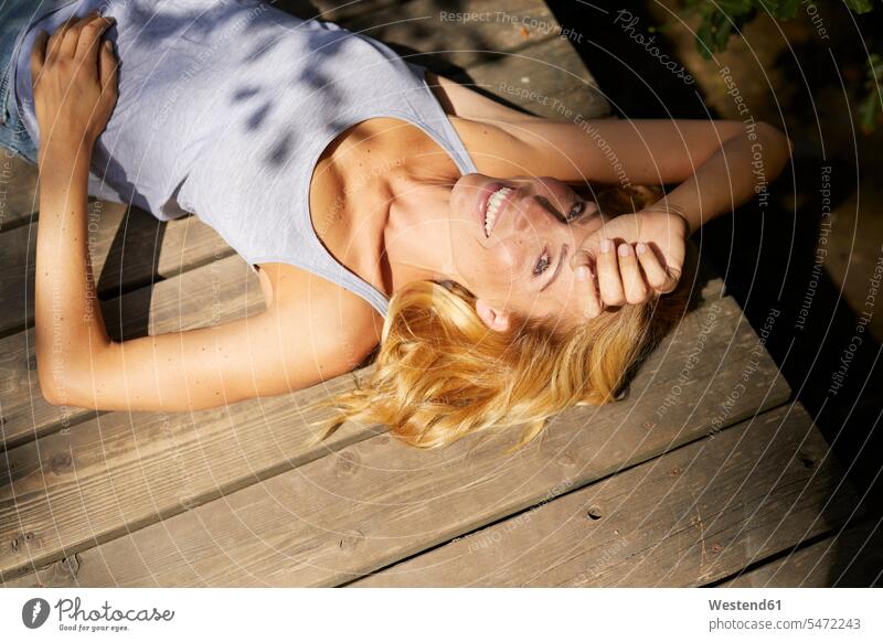 Glückliche blonde Frau liegt auf Holzsteg in der Sonne Sonnenlicht glücklich glücklich sein glücklichsein liegen liegend Steg Stege Anlegestelle blonde Haare