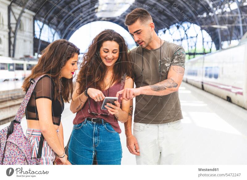 Freunde mit Handy auf dem Bahnsteig Zugbahnsteig Zugbahnsteige Bahnsteige Bahnhof Bahnhofsgebäude glücklich Glück glücklich sein glücklichsein Mobiltelefon